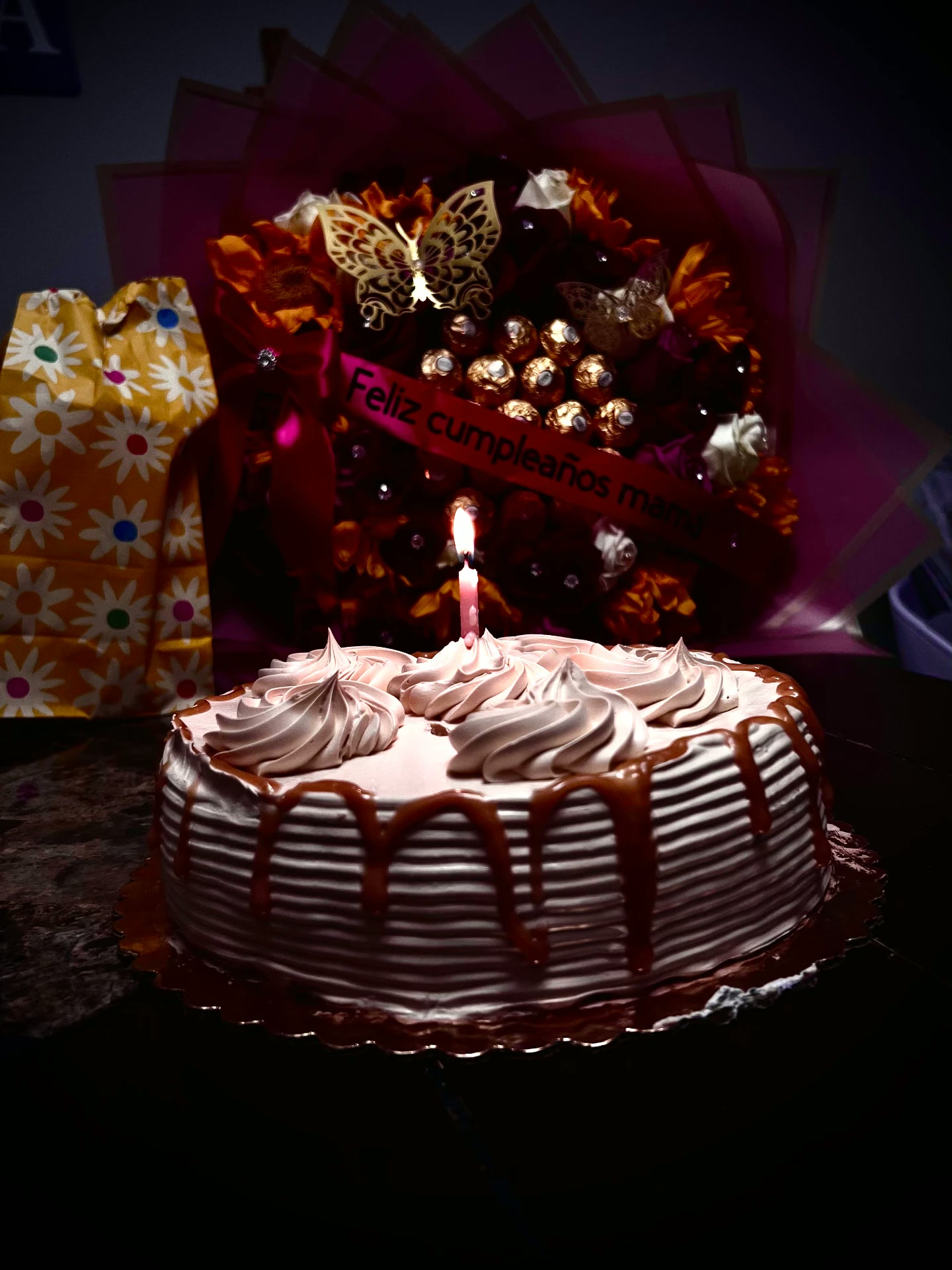 Caramel drip birthday cake with a lit candle and Ferrero Rocher gift arrangement